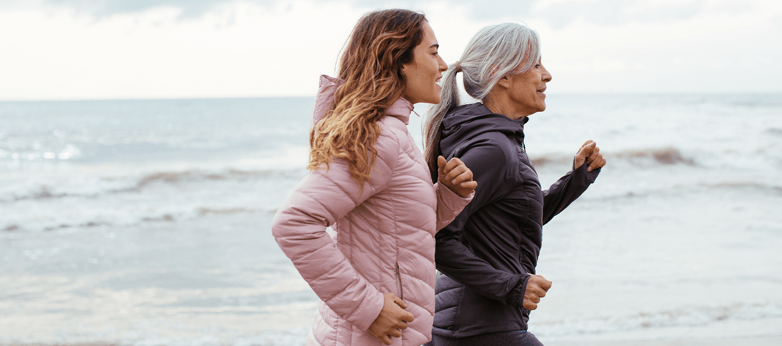 Older mother and daughter power walking on beach